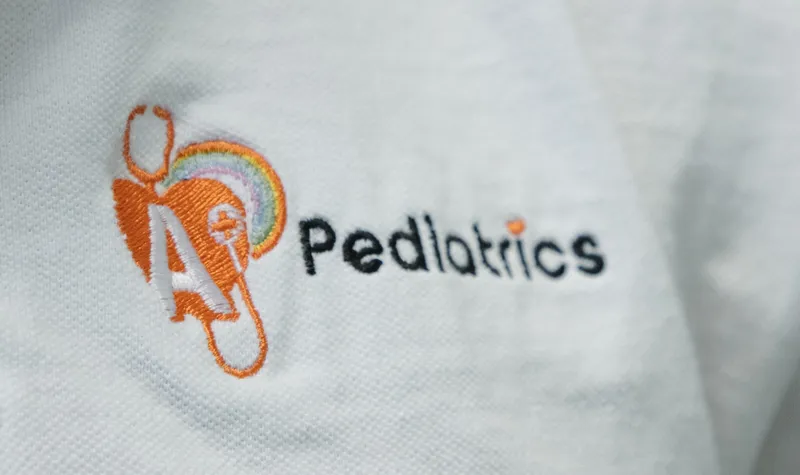 The A+ Pediatrics logo embroidered on a clinic polo shirt