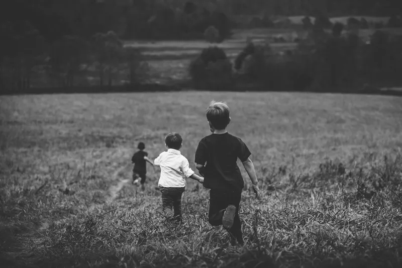 Three children running across a rural field, seen from behind